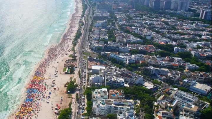 Vista aérea da praia e bairros na Barra da Tijuca em dia ensolarado.
