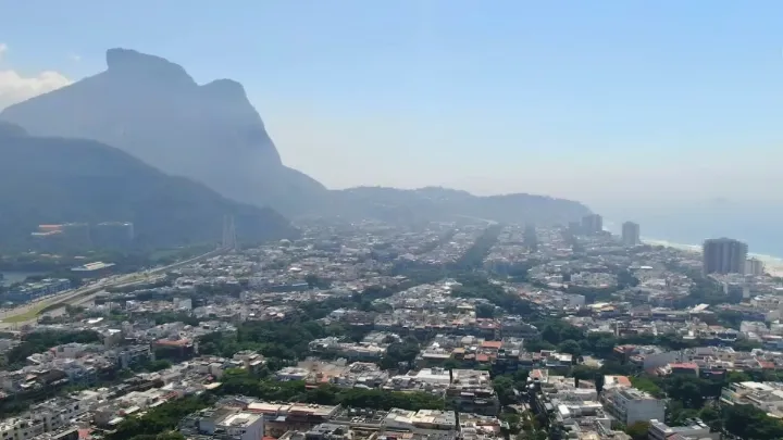 Vista aérea ampla da Barra da Tijuca com montanhas e prédios ao fundo.