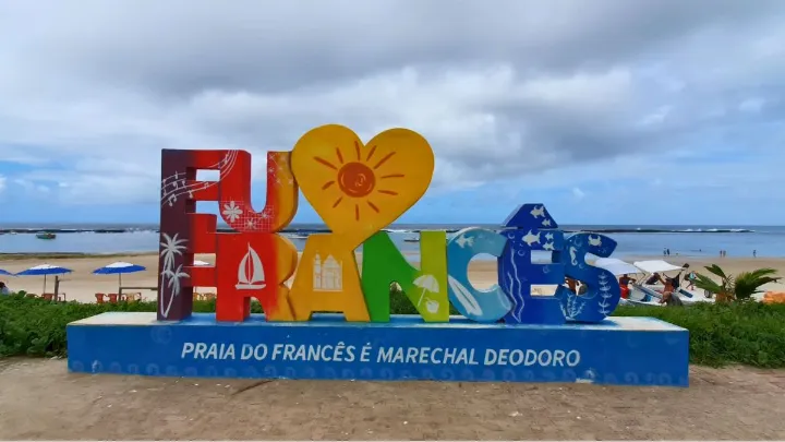Letreiro colorido com texto Eu amo Francês na Praia do Francês, com mar ao fundo.