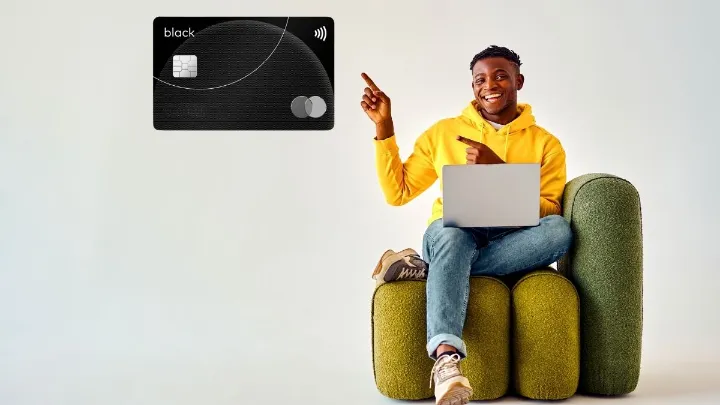 Homem em assento verde com laptop apontando para cartão Mastercard Black exibido ao lado.