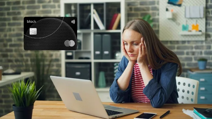 Mulher com expressão frustrada olhando para laptop, cartão preto flutuando ao lado.