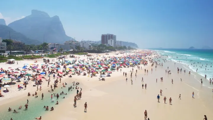 Vista aérea da Praia da Barra da Tijuca com guarda-sóis e muitas pessoas.