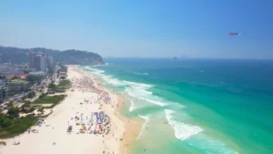 Praia com mar calmo e faixa de areia larga na Barra da Tijuca, vista aérea.