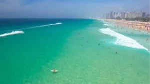 Vista aérea de uma praia na Barra da Tijuca com mar azul e pessoas na areia