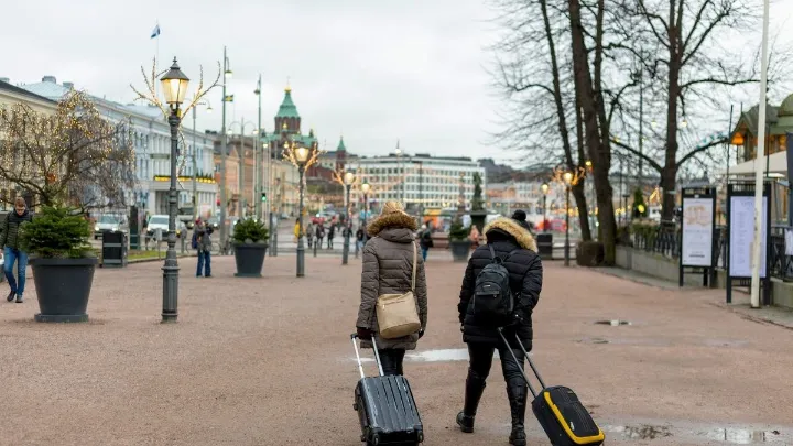Duas pessoas com malas andando em uma rua arborizada em clima frio.