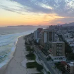 Vista aérea da praia da Barra da Tijuca com prédios e mar ao amanhecer.
