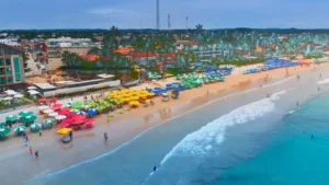 Vista aérea de uma praia com guarda-sóis coloridos, pessoas e mar calmo em Porto de Galinhas.