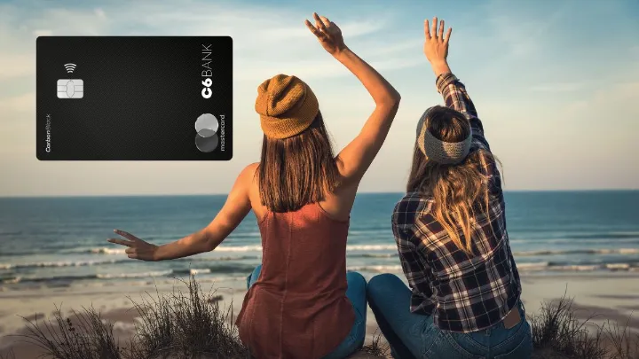 Cartão Mastercard Black C6 Bank em destaque ao lado de duas pessoas na praia.