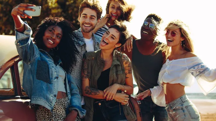 Grupo de amigos sorrindo e tirando uma selfie ao ar livre.
