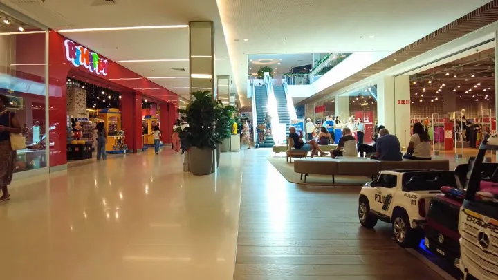 Corredor de shopping na Barra da Tijuca com lojas, escada rolante e pessoas.