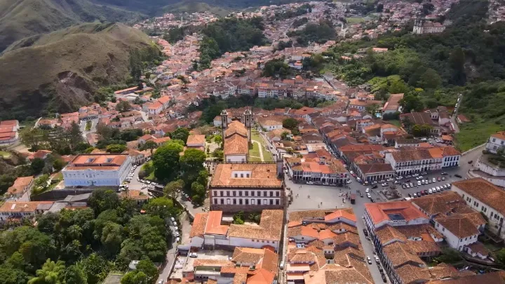 Vista aérea de cidade histórica em Minas Gerais com telhados coloniais, igreja ao centro, ruas movimentadas e montanhas ao redor
